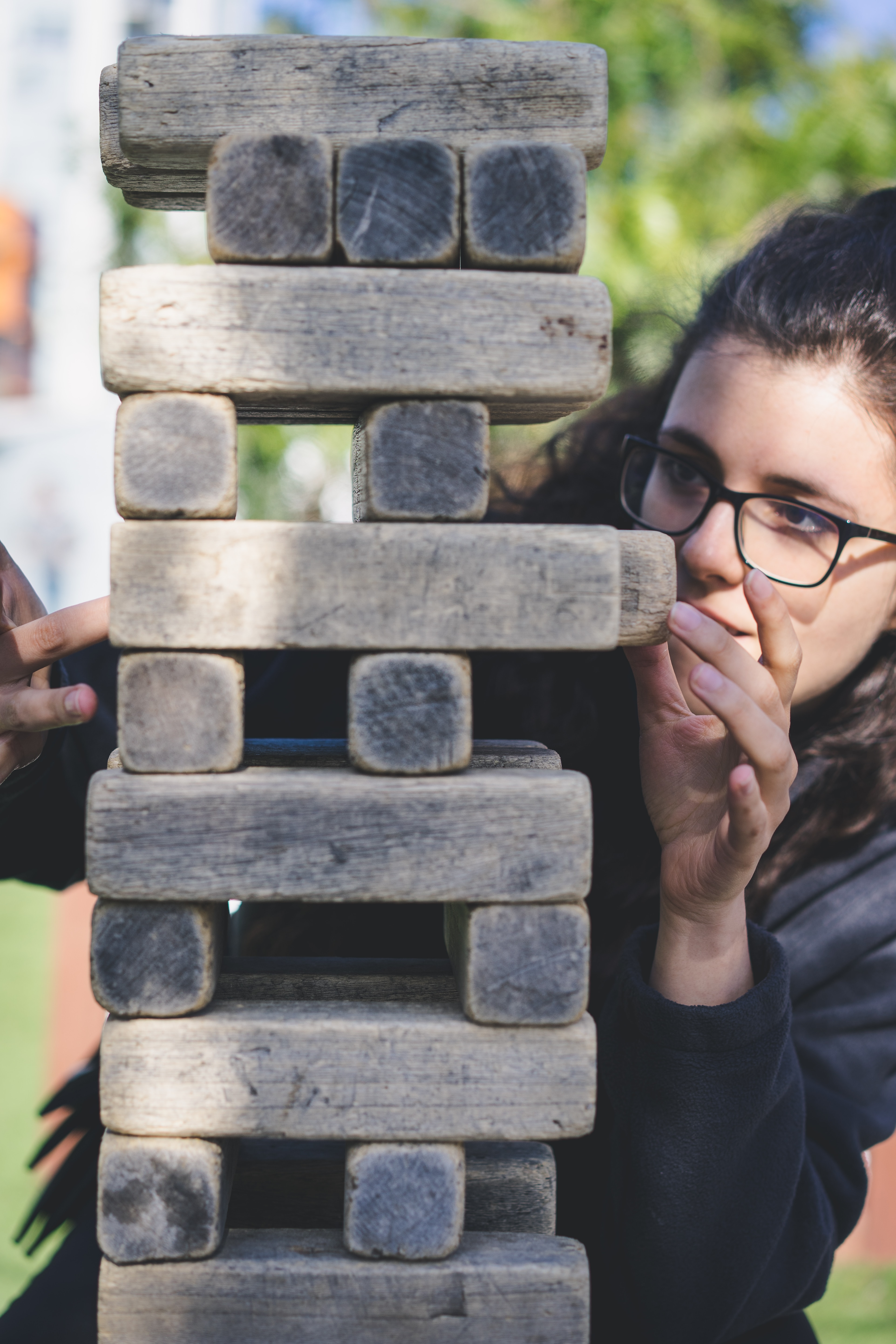 Lady with glasses pulling out a jenga block from the middle of a jenga tower